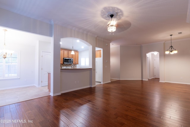 unfurnished living room featuring arched walkways, dark wood finished floors, ornamental molding, and ceiling fan with notable chandelier