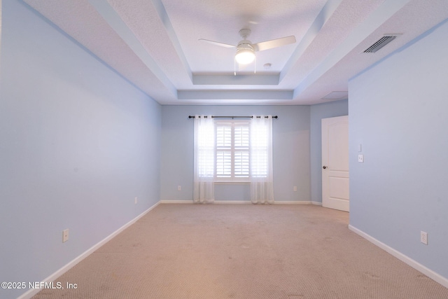 unfurnished room featuring ceiling fan, light carpet, a tray ceiling, and visible vents