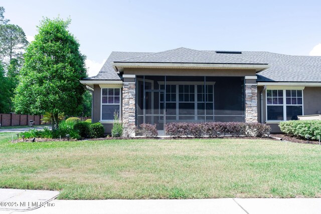 prairie-style house with a sunroom, roof with shingles, a front yard, and stone siding