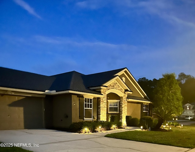 ranch-style home with a garage, stucco siding, driveway, and stone siding