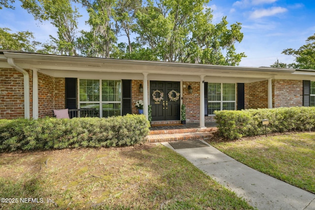 entrance to property featuring a porch, brick siding, and a lawn