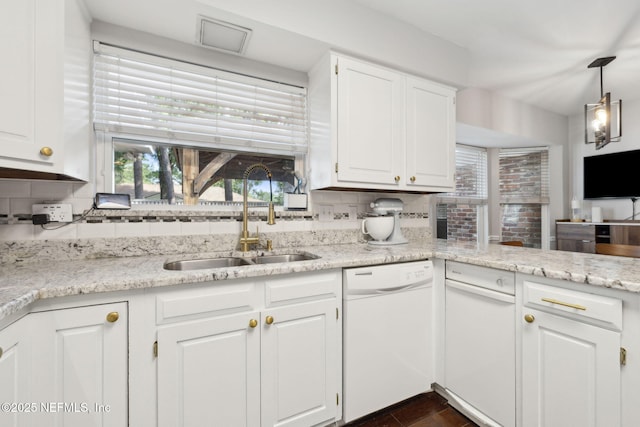 kitchen with white dishwasher, tasteful backsplash, light stone countertops, a sink, and white cabinets
