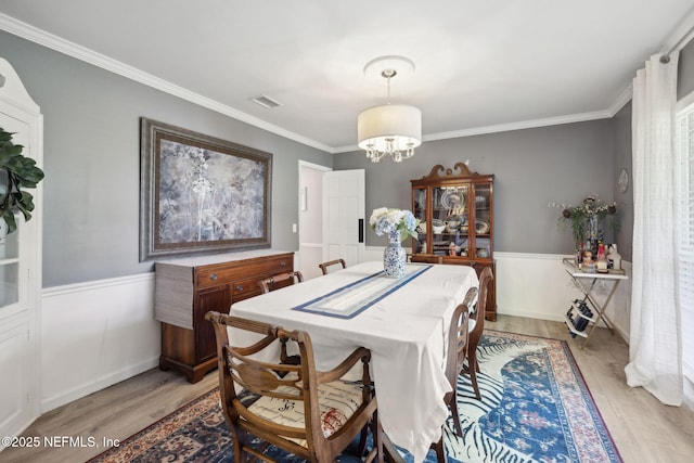 dining space featuring wainscoting, light wood finished floors, a chandelier, visible vents, and ornamental molding