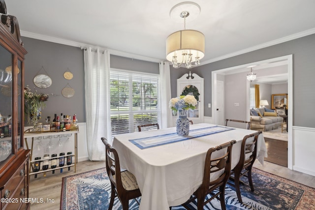 dining room with wainscoting, an inviting chandelier, ornamental molding, and light wood-style floors