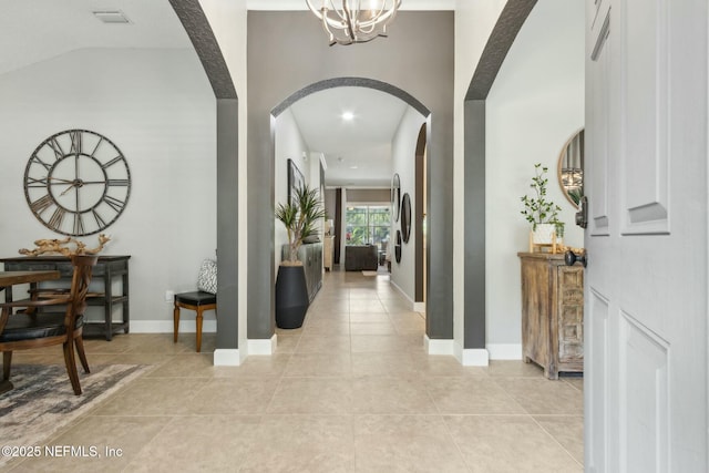 hallway featuring a chandelier, light tile patterned flooring, visible vents, baseboards, and arched walkways