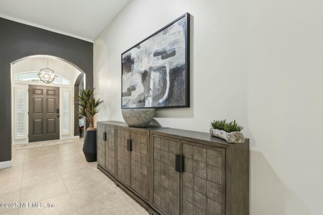 hall featuring arched walkways, light tile patterned floors, and an inviting chandelier