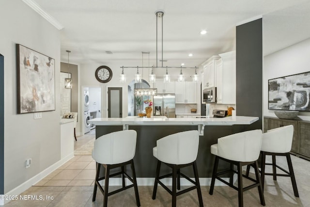 kitchen featuring stainless steel appliances, stacked washer and clothes dryer, a peninsula, light countertops, and white cabinets