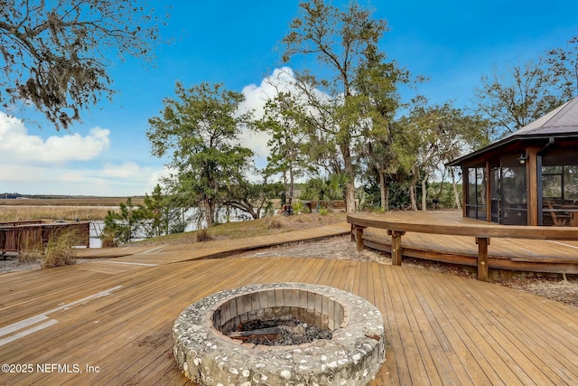 wooden deck featuring an outdoor fire pit and a sunroom