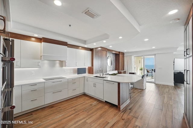 kitchen with a sink, dishwasher, a peninsula, light wood-style flooring, and recessed lighting