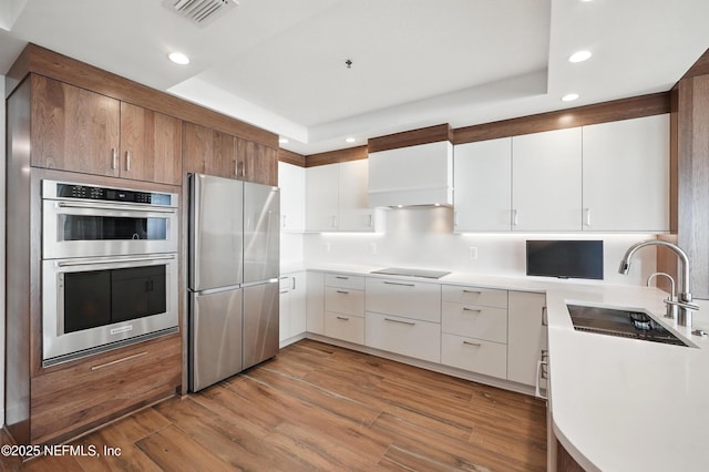 kitchen featuring stainless steel appliances, a sink, recessed lighting, light countertops, and a tray ceiling