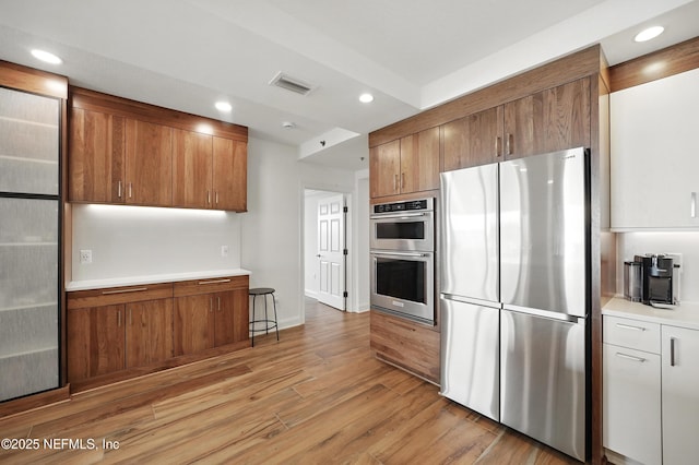 kitchen with appliances with stainless steel finishes, brown cabinets, light wood-type flooring, light countertops, and recessed lighting