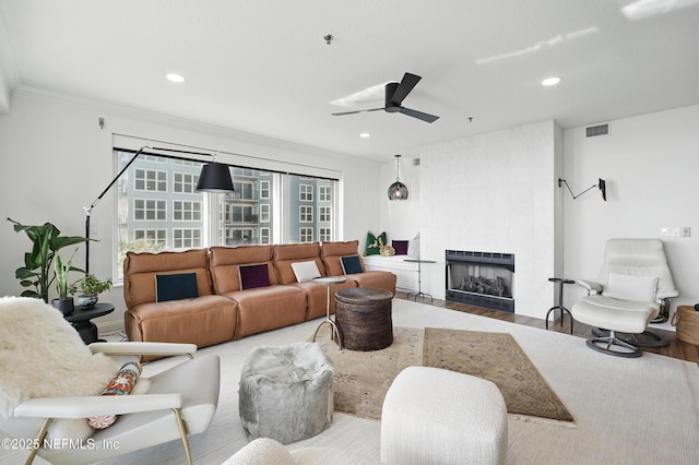 living area with a ceiling fan, wood finished floors, a fireplace, recessed lighting, and crown molding