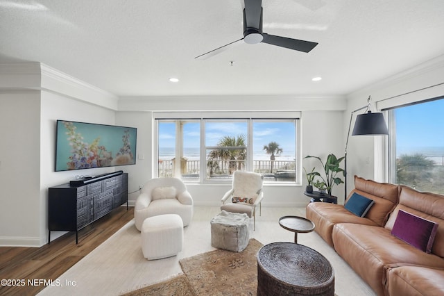 living room featuring wood finished floors, healthy amount of natural light, crown molding, baseboards, and ceiling fan