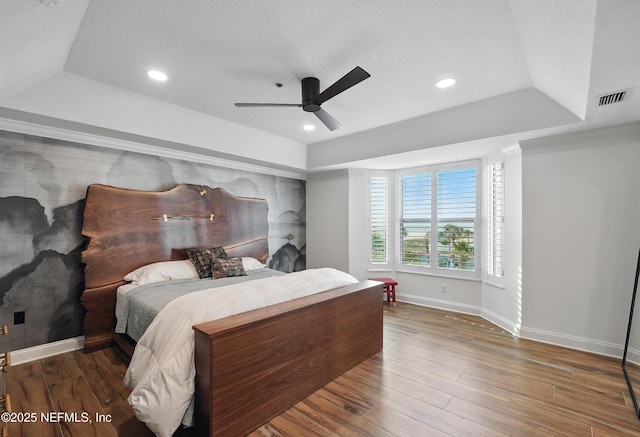 bedroom featuring a tray ceiling, baseboards, wood finished floors, and recessed lighting