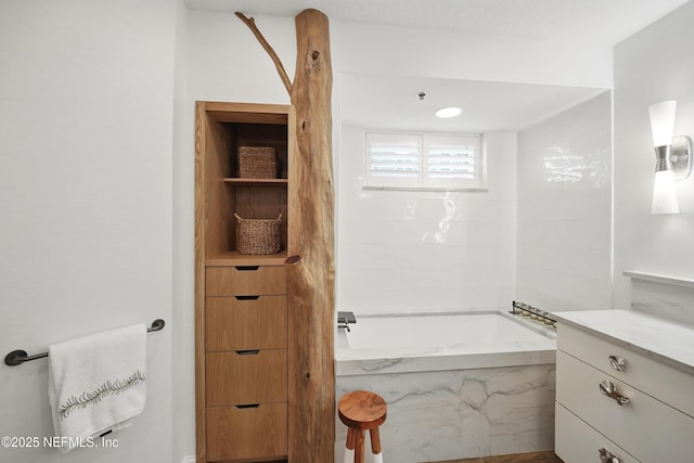 bathroom with a tub with marble appearance and vanity