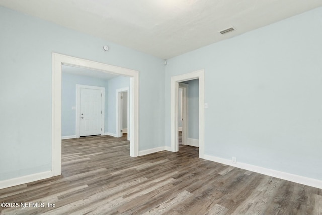 unfurnished room with baseboards, wood finished floors, and visible vents