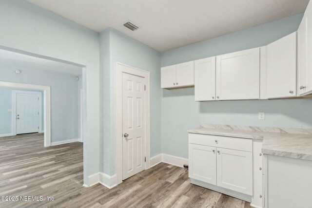kitchen with light wood finished floors, light countertops, white cabinets, baseboards, and visible vents
