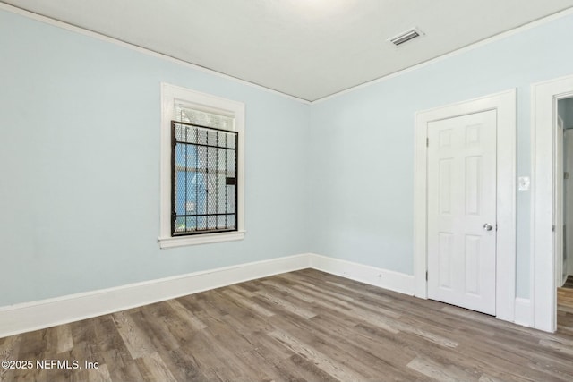empty room with baseboards, crown molding, and wood finished floors