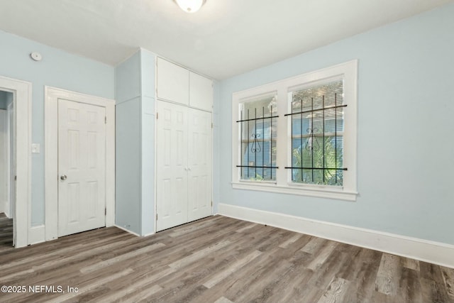 unfurnished bedroom featuring wood finished floors, a closet, and baseboards
