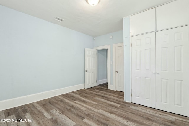 unfurnished bedroom with visible vents, baseboards, wood finished floors, and a closet