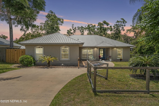 single story home featuring metal roof, fence, a front lawn, concrete driveway, and stucco siding