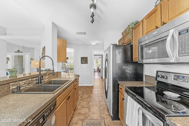 kitchen featuring brown cabinetry, baseboards, a sink, light tile patterned floors, and stainless steel appliances