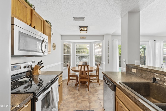 kitchen featuring visible vents, dark countertops, brown cabinets, a sink, and stainless steel appliances