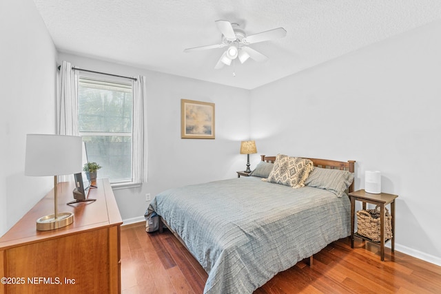 bedroom featuring ceiling fan, a textured ceiling, baseboards, and wood finished floors