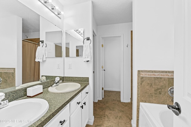 bathroom with a sink, a bathing tub, double vanity, and a textured ceiling