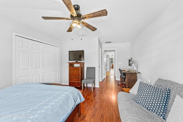bedroom with a ceiling fan, a textured ceiling, visible vents, wood finished floors, and a closet