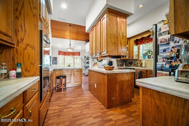 kitchen featuring brown cabinets, decorative light fixtures, a peninsula, light countertops, and double oven