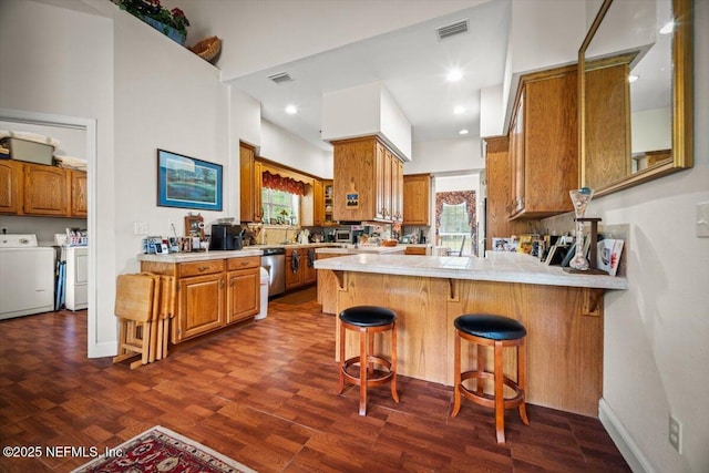 kitchen featuring independent washer and dryer, visible vents, dark wood-style floors, a peninsula, and brown cabinetry