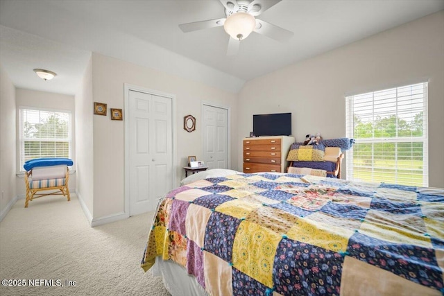 bedroom featuring lofted ceiling, baseboards, light carpet, multiple closets, and a ceiling fan