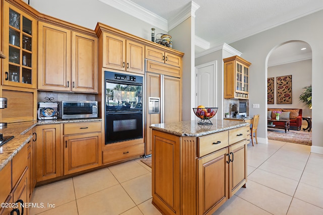 kitchen featuring stainless steel microwave, a center island, paneled built in refrigerator, arched walkways, and dobule oven black