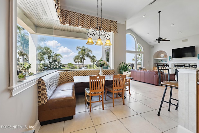 tiled dining room featuring a fireplace, built in features, lofted ceiling, and ceiling fan with notable chandelier