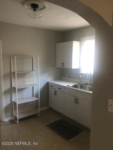kitchen featuring arched walkways, a sink, white cabinetry, light countertops, and light tile patterned floors