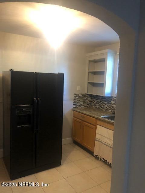 kitchen with dark countertops, tasteful backsplash, light tile patterned flooring, arched walkways, and black fridge