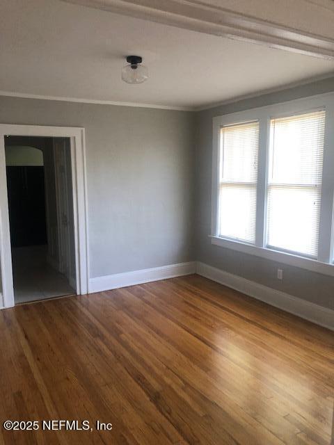 spare room featuring wood finished floors, crown molding, and baseboards