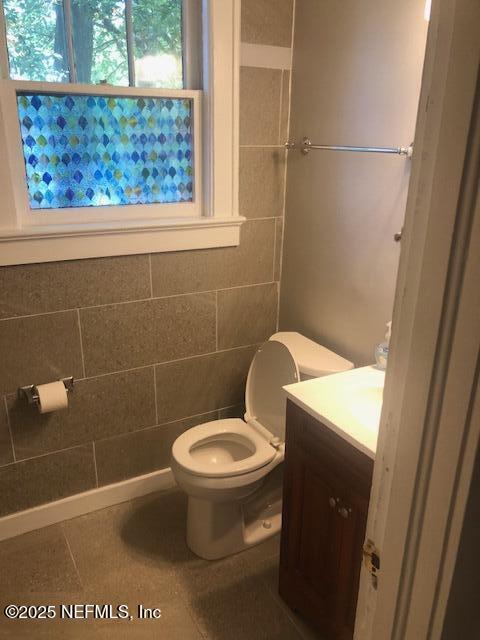 bathroom featuring toilet, vanity, tile patterned floors, and tile walls