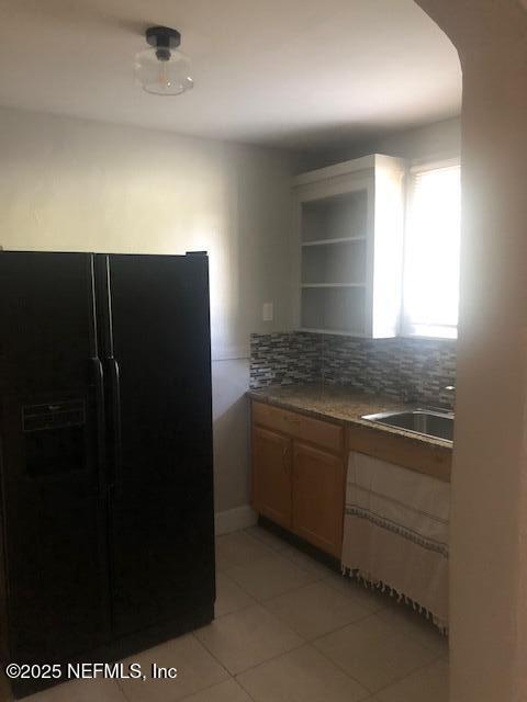 kitchen with arched walkways, a sink, tasteful backsplash, black refrigerator with ice dispenser, and light tile patterned floors