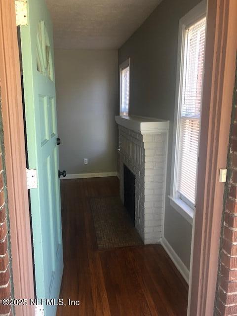 unfurnished living room with baseboards, a brick fireplace, and wood finished floors