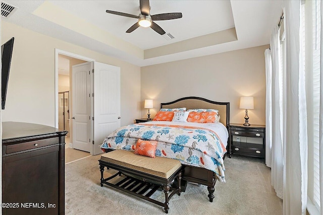 bedroom with a raised ceiling, light colored carpet, and visible vents