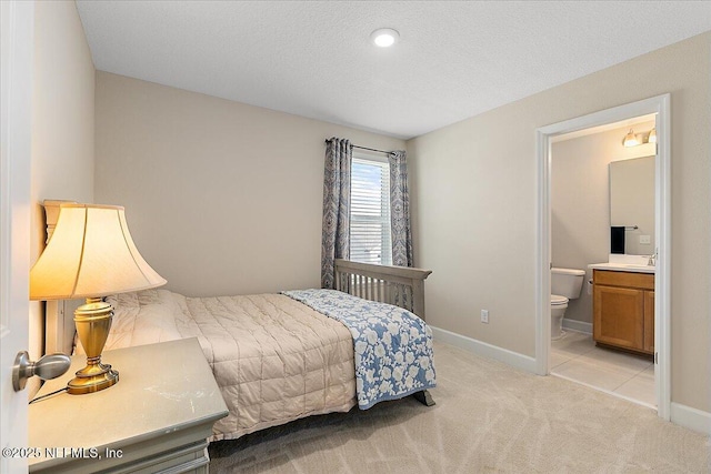 bedroom featuring baseboards, a sink, connected bathroom, and light carpet