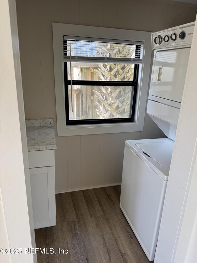 clothes washing area with stacked washer / dryer, cabinet space, a decorative wall, and dark wood finished floors
