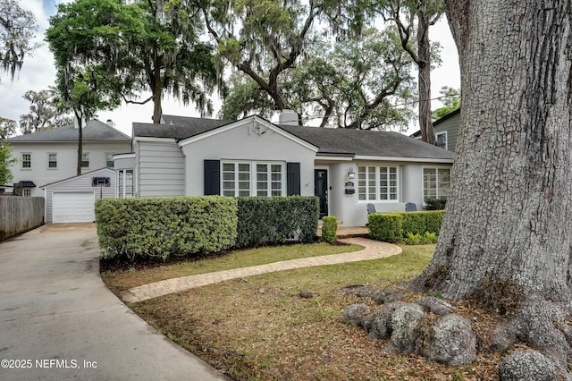 view of front facade featuring a garage, an outbuilding, concrete driveway, stucco siding, and fence