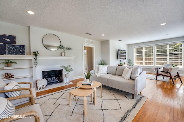 living room featuring a fireplace with flush hearth, a textured ceiling, visible vents, light wood-type flooring, and recessed lighting
