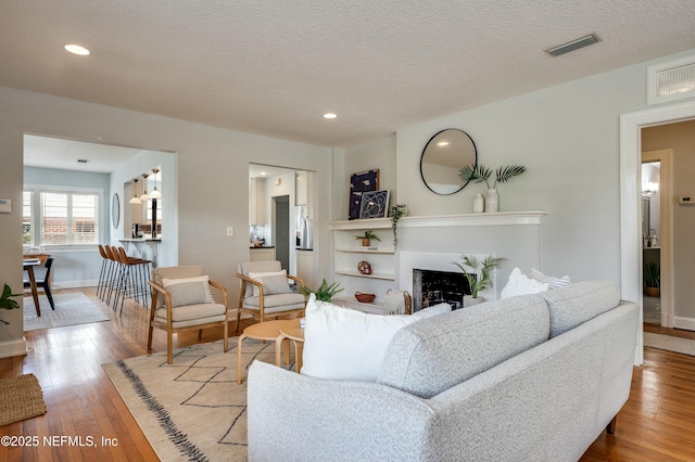 living room with recessed lighting, visible vents, wood finished floors, and a fireplace