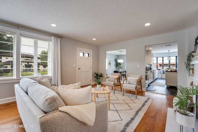 living area with recessed lighting, a textured ceiling, light wood-style flooring, and baseboards
