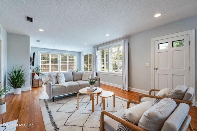 living room with a textured ceiling, visible vents, recessed lighting, and baseboards