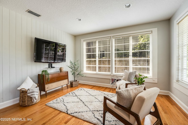 living area with a textured ceiling, visible vents, wood finished floors, and baseboards